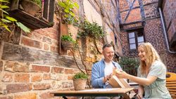 Zwei Personen sitzen an einem Tisch in einem Innenhof der Celler Altstadt und genießen einen Snack in entspannter Atmosphäre.