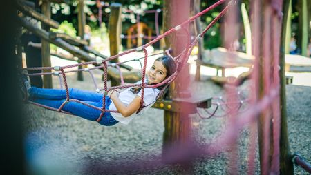 Mädchen auf roten Kletterseilen im Schlosspark Celle, umgeben von Spielgerüsten und Bäumen, lachend und spielend auf dem familienfreundlichen Spielplatz
