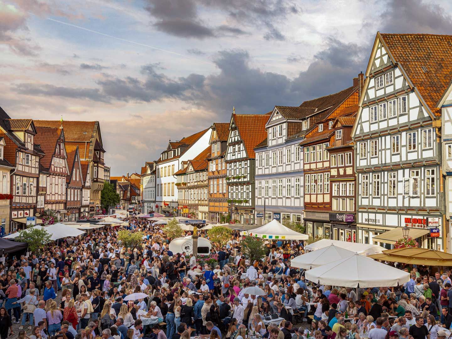 Belebter Celler Weinmarkt mit vielen Besuchern, umgeben von traditionellen Fachwerkhäusern und großen Schirmen.