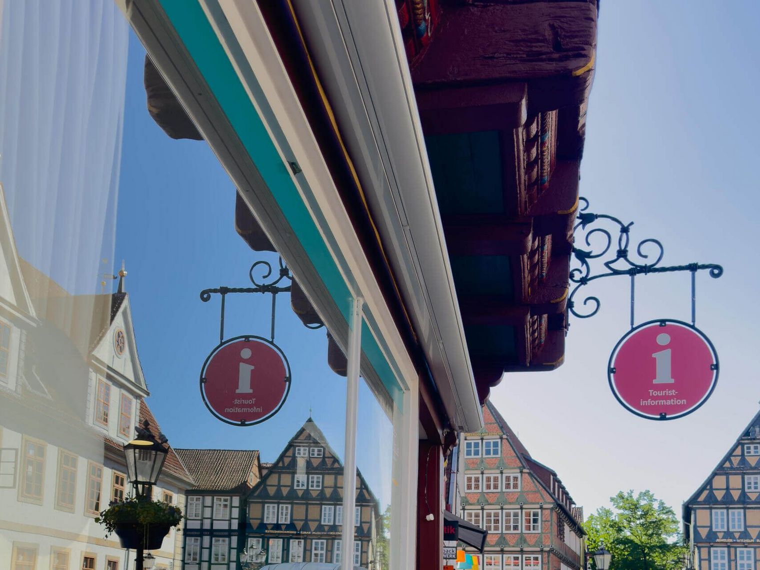 Historisches Fachwerkhaus mit Tourist-Information in Celle, in dessen Fenster sich das Alte Rathaus spiegelt.